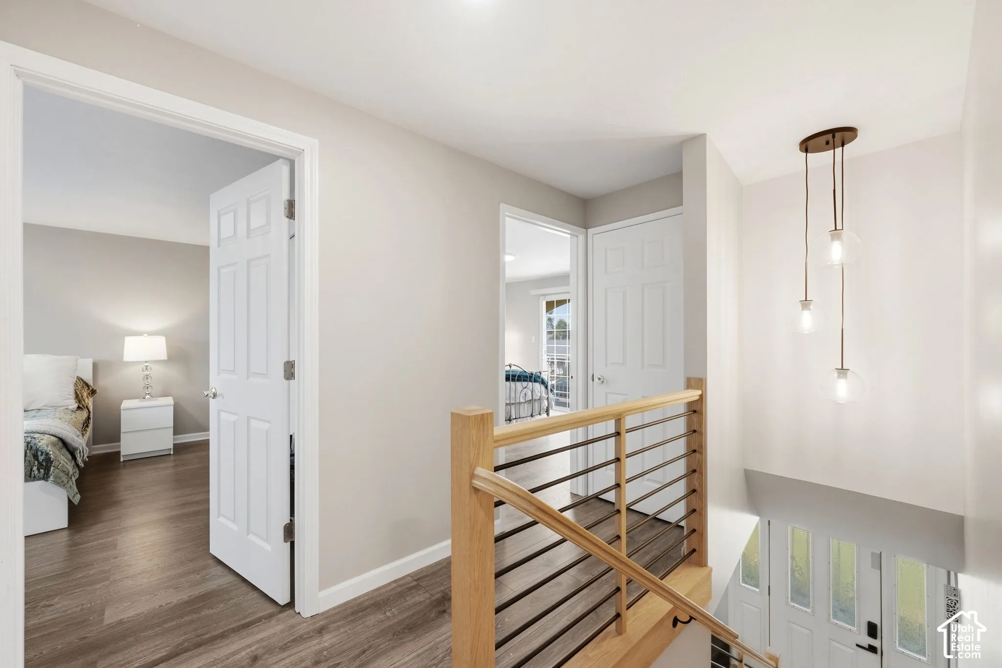 Open hallway with wood-finish flooring, light neutral wall tones, and a modern pendant light fixture