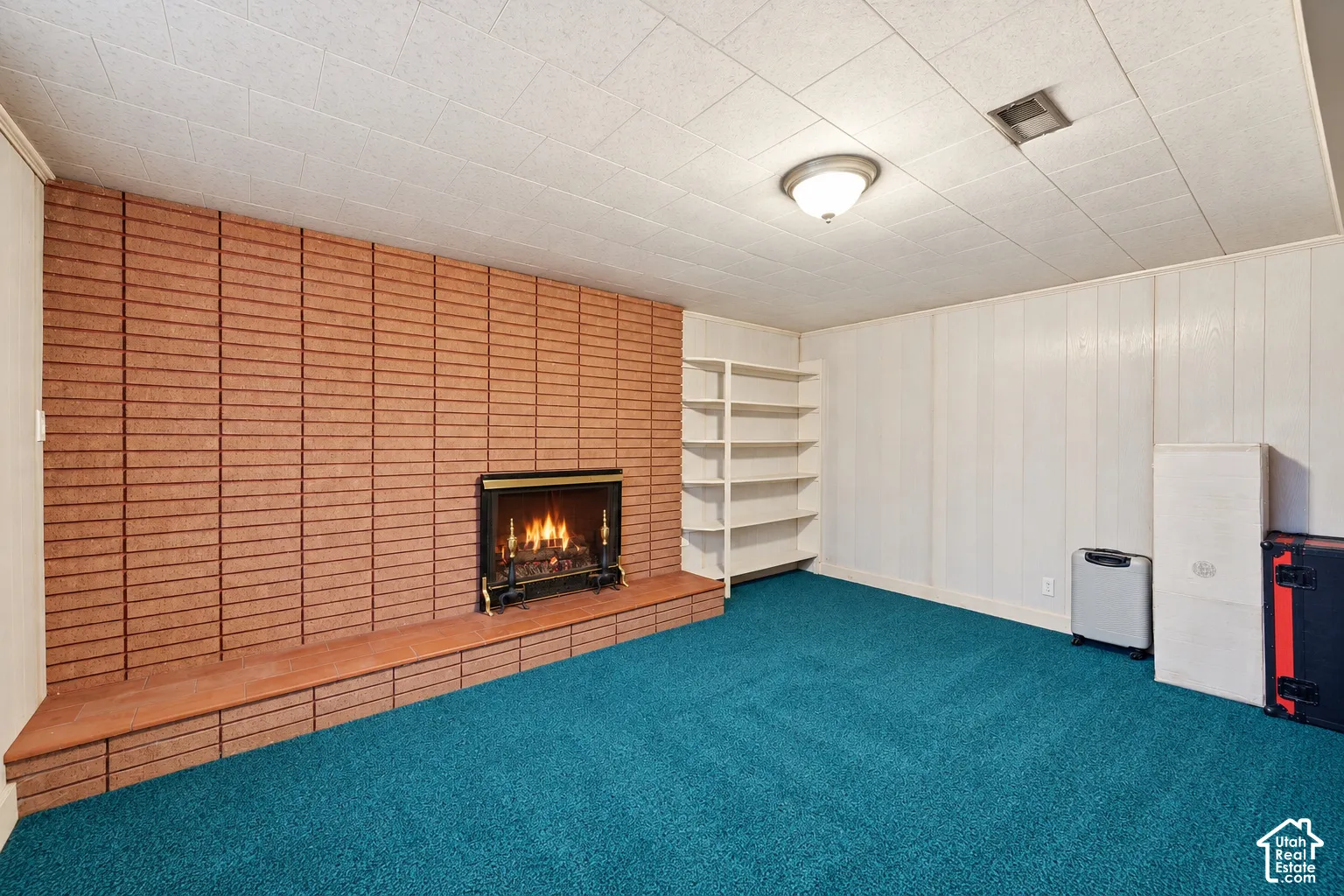 Brick fireplace with a hearth, wall-to-wall carpeting, wood paneling, built-in shelving, and a flush mount light fixture
