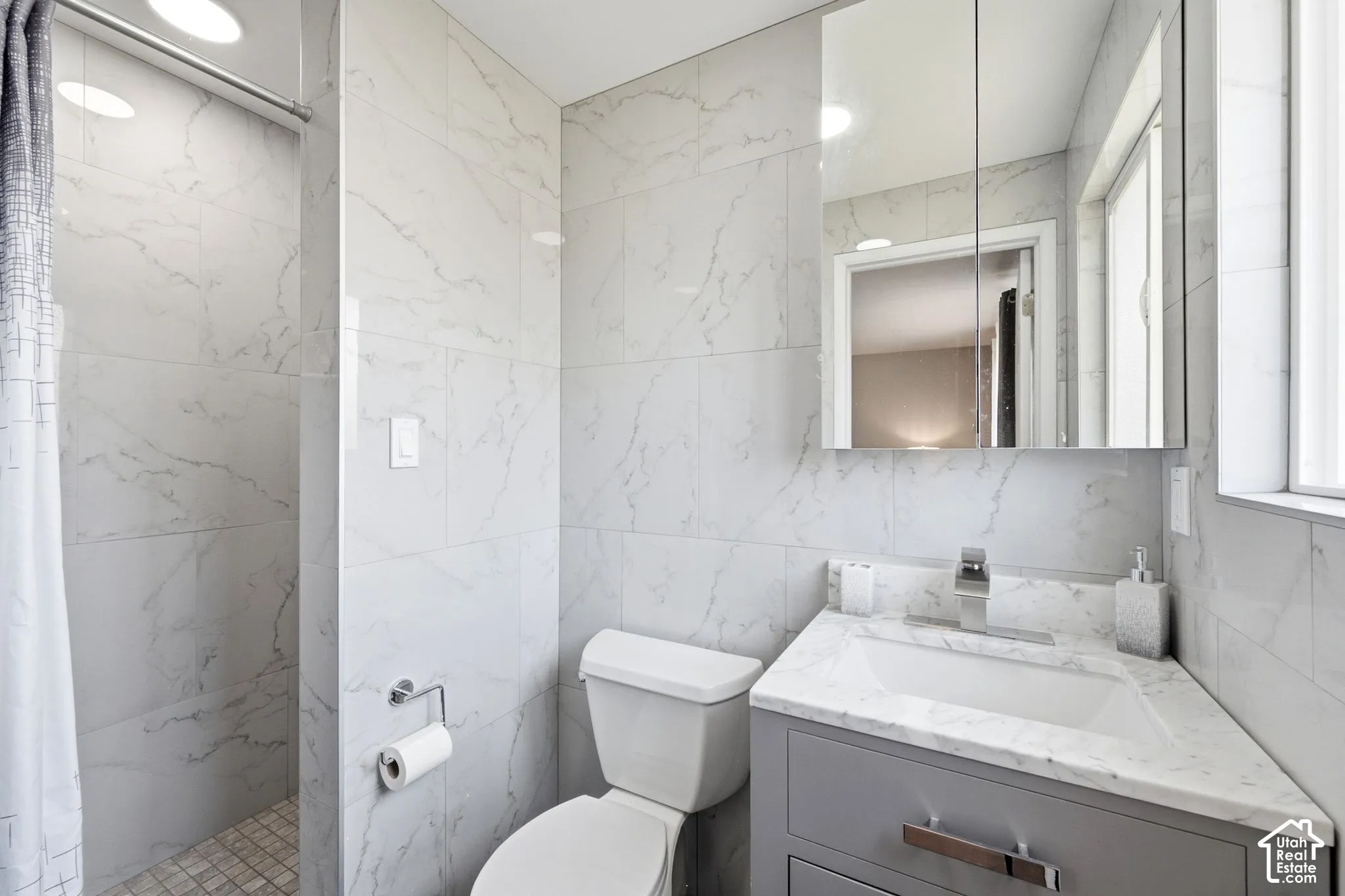 Shower with mosaic tile floor, white subway tile walls, corner vanity with integrated sink, chrome faucet, and mirrored medicine cabinet