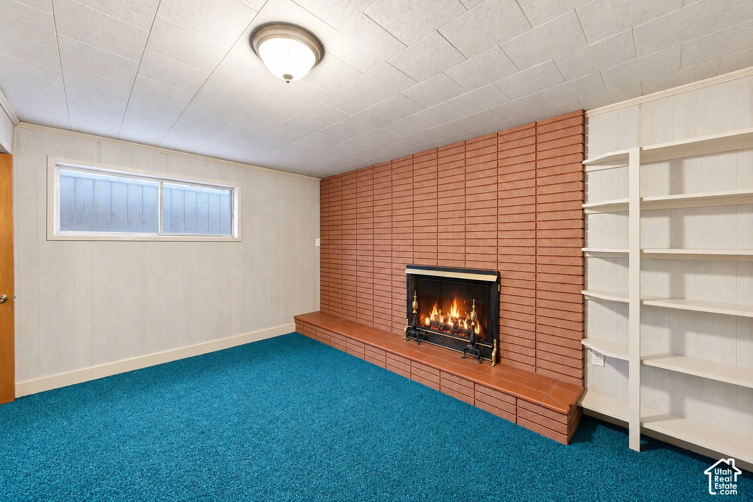 Brick fireplace with a tiled hearth, built-in shelving, a drop ceiling, and a flush-mount light fixture