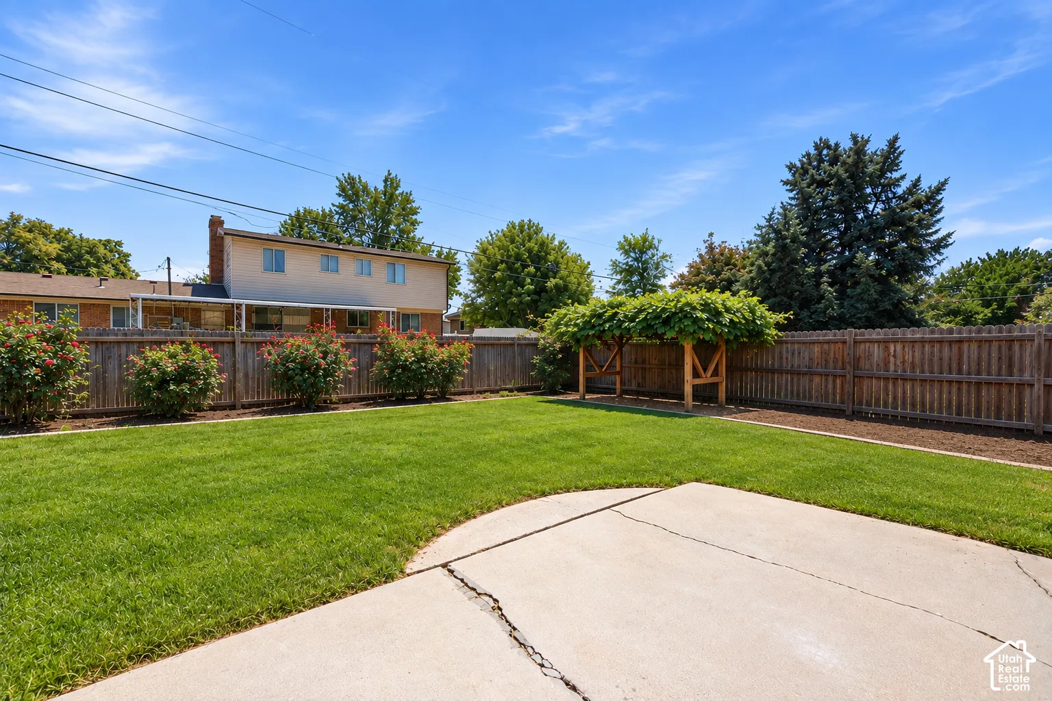 Expansive lawn with a concrete patio, wood privacy fencing, and a built-in wood pergola structure