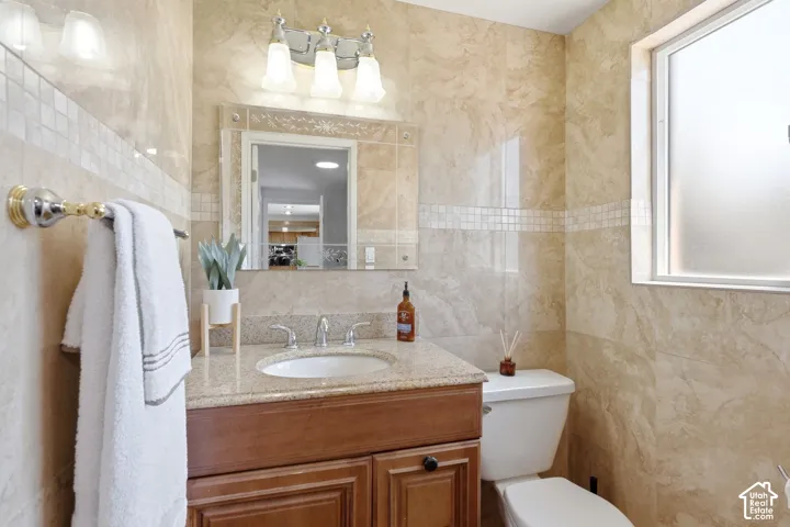 Bathroom featuring full-height tiled walls, a vanity with a granite countertop, an undermount sink, and a wall-mounted light fixture