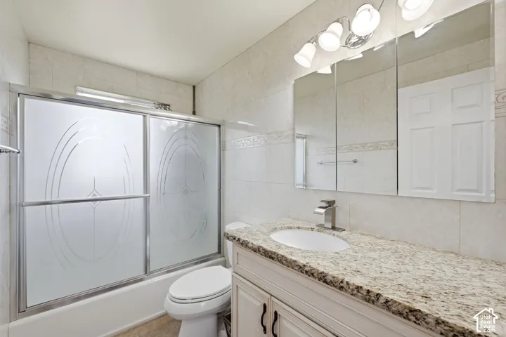 Bathroom featuring a white vanity with a light-colored countertop, an undermount sink with a chrome faucet, a mirrored medicine cabinet, and a bathtub with frosted glass sliding doors