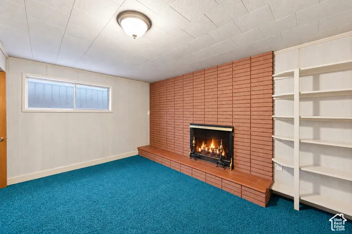Brick fireplace with a tiled hearth, built-in shelving, a drop ceiling, and a flush-mount light fixture