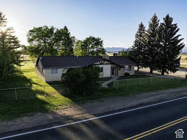 Single-story residence featuring a stone and stucco exterior, dark roof, and mature perimeter trees