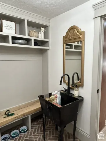 Built-in storage cubbies, decorative wall mirror, utility sink with a black fixture, wood bench, and herringbone brick flooring