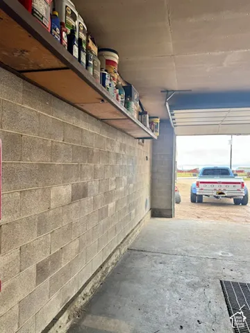 Cinder block wall construction, concrete flooring, overhead shelving, industrial garage door, and floor drain