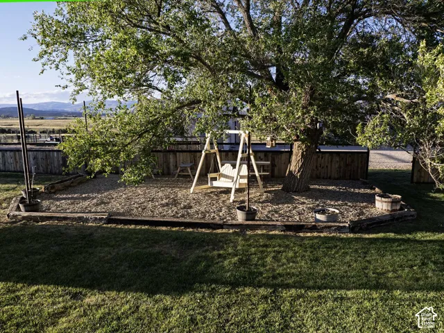 Expansive outdoor area featuring a large mature tree, defined gravel ground cover, a wooden privacy fence, and distant mountain scenery