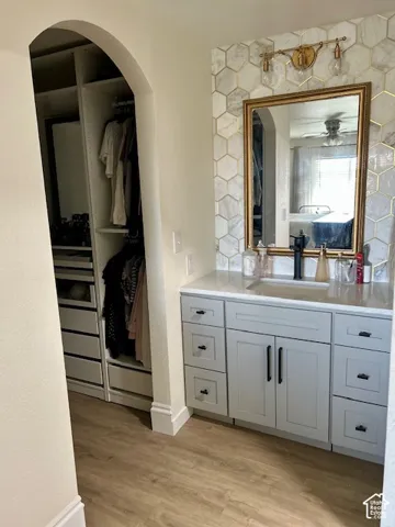 Built-in closet system, arched doorway, hexagon tile accent wall, vanity with undermount sink, wood-finish flooring