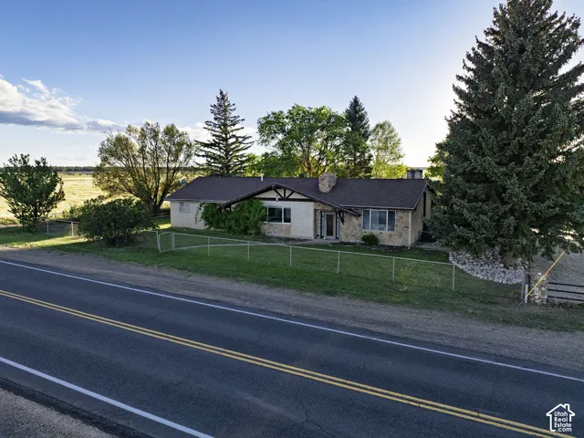 Ranch-style exterior with stone and stucco finishes, a prominent chimney, dark shingle roofing, and a front yard featuring mature trees and a chain-link fence