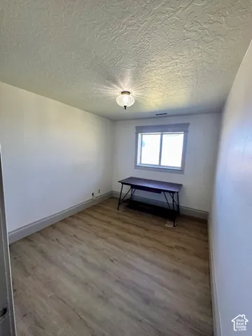 Wood-finish flooring with light-toned walls, featuring a window with trim and a ceiling-mounted light fixture