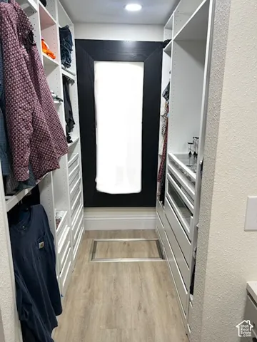 Built-in closet system with shelving and drawers, wood-finish flooring, and recessed lighting