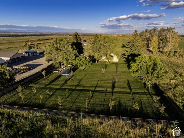 Expansive green space with perimeter fencing, mature trees, young trees, and distant mountain scenery