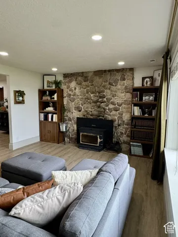 Stone-faced fireplace with wood stove insert, wood-finish flooring, recessed lighting, and built-in shelving