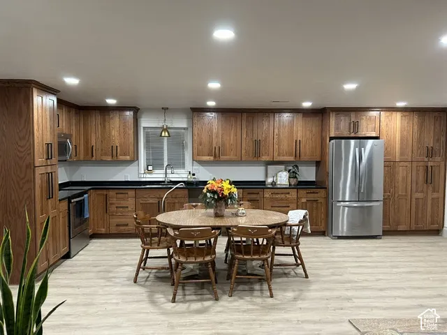 Expansive kitchen featuring wood cabinetry, dark countertops, stainless steel appliances, and light wood-finish flooring