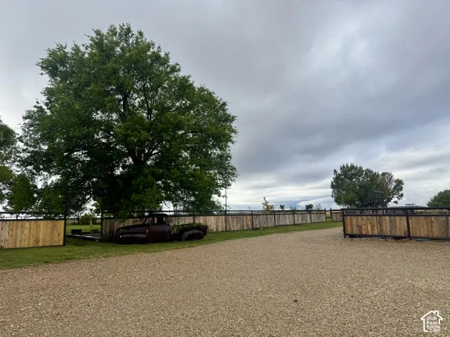 Expansive gravel driveway bordered by a wooden fence, featuring mature trees and a rustic ornamental truck