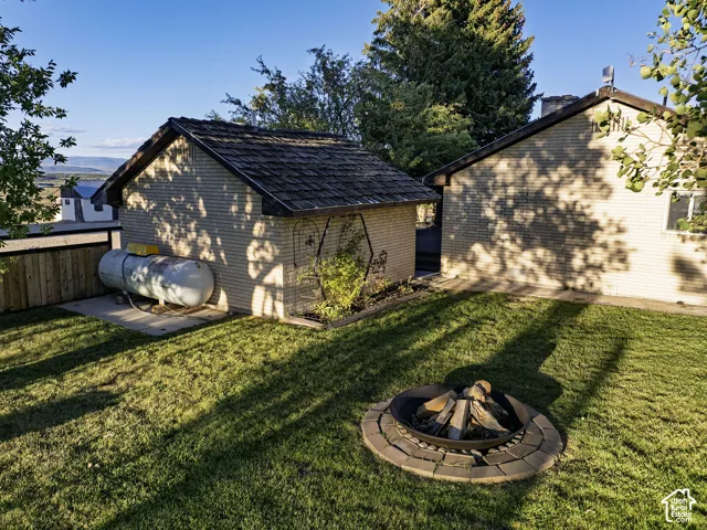 Expansive grassy yard featuring a stone-lined fire pit, a detached brick outbuilding with a shingle roof, and a privacy fence