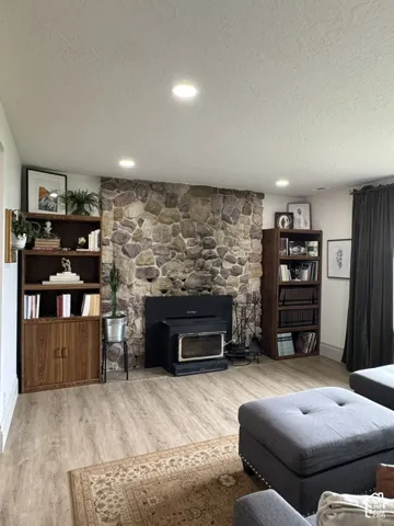 Stone-clad fireplace with a wood-burning insert, wood-finish flooring, recessed lighting, and dark window treatments