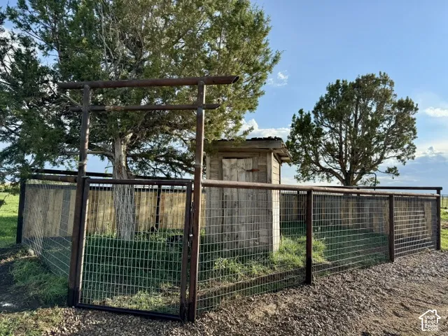 Wire mesh fencing enclosing a grassy area with mature trees and a rustic wood structure