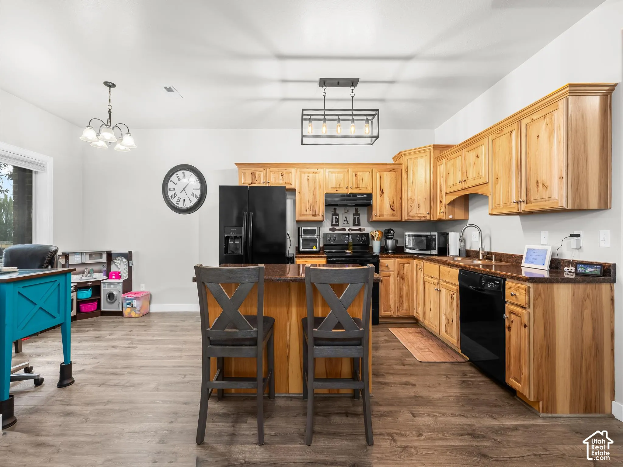 Kitchen featuring wood cabinetry, dark countertops, black appliances, a central island, and wood-finish flooring