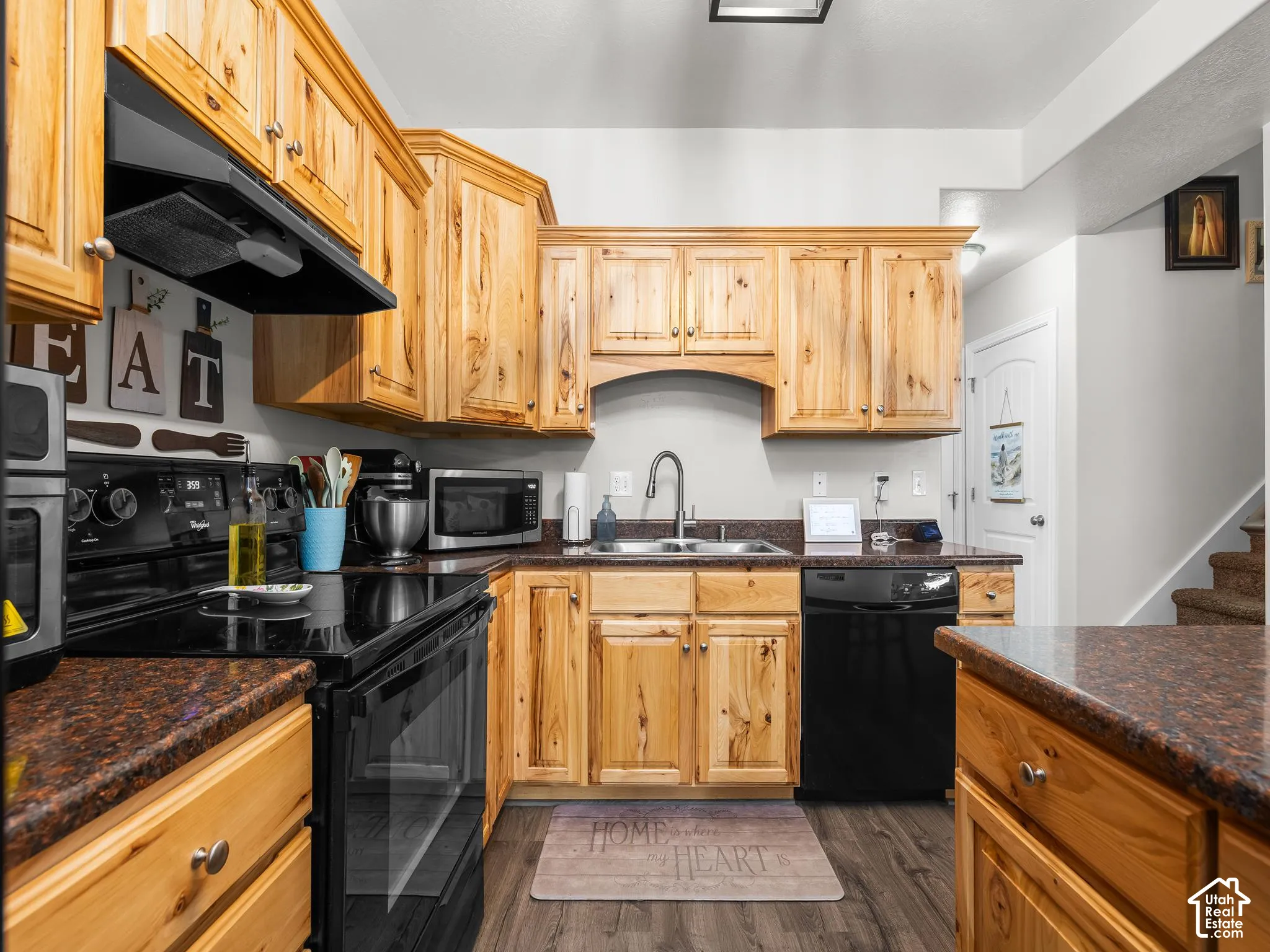 Kitchen featuring wood cabinetry, dark countertops, a stainless steel sink, black appliances, and wood-finish flooring