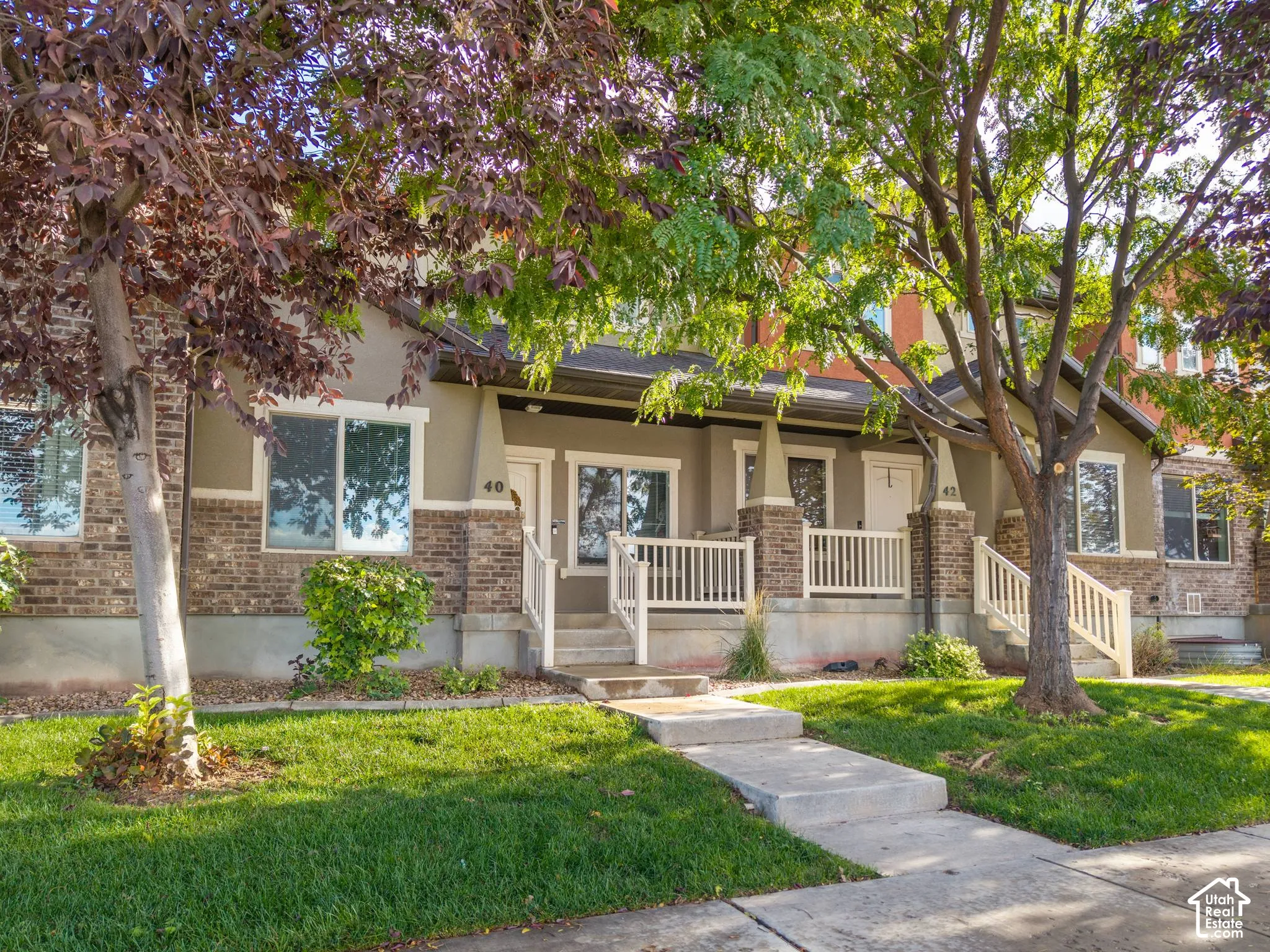 Two-story residence featuring brick and stucco exterior, covered front porch with white railings, and mature trees
