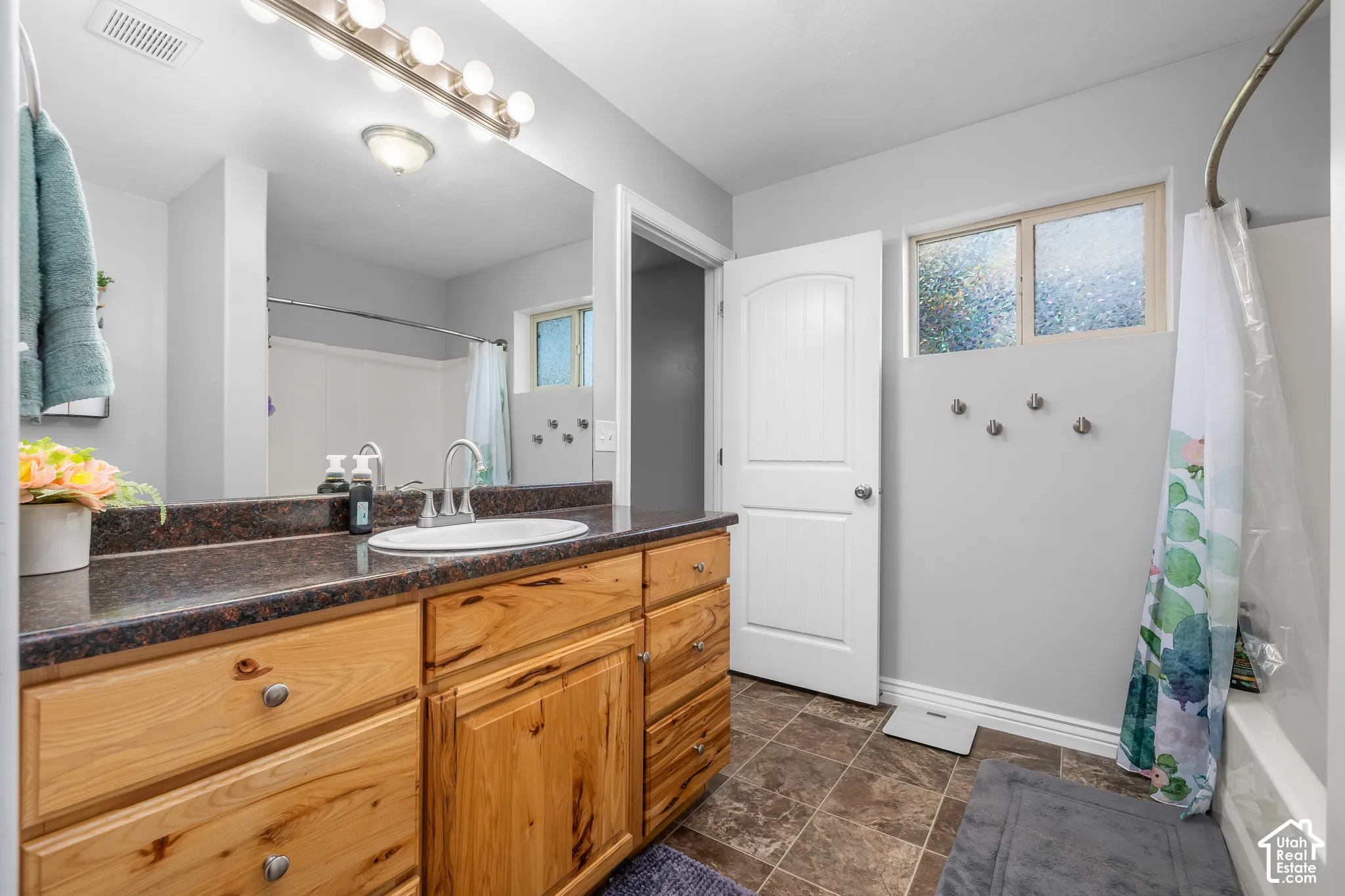 Bathroom featuring a vanity with a single basin, wood-finish cabinetry, a dark countertop, and a built-in bathtub with shower