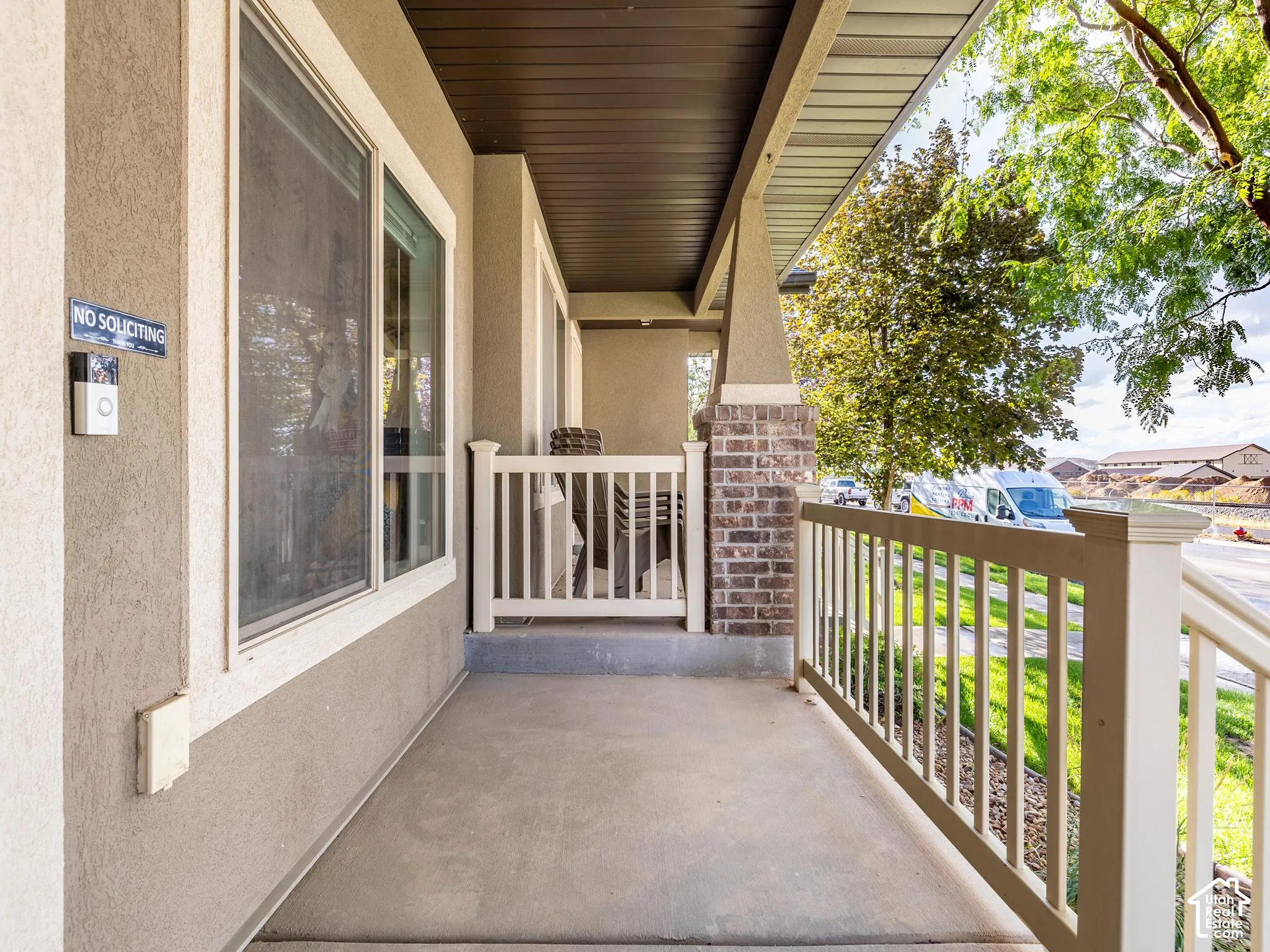 Covered front porch featuring a concrete floor, stucco exterior, and white railing