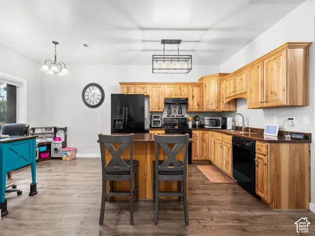 Kitchen featuring wood cabinetry, dark countertops, black appliances, a central island, and wood-finish flooring