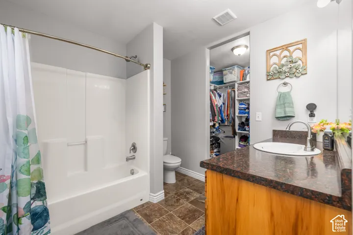 White tub-shower combination, wood-finish vanity with a dark countertop, undermount sink, and a walk-in closet with built-in shelving