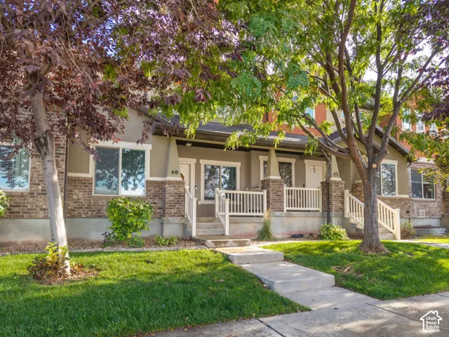 Two-story residence featuring brick and stucco exterior, covered front porch with white railings, and mature trees