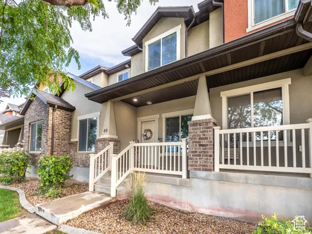 Exterior featuring brick accents, stucco siding, a covered front porch, white railing, and an entry door
