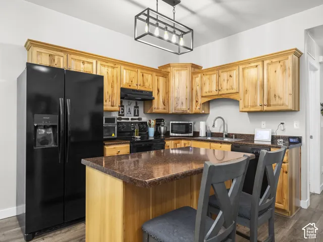 Well-appointed kitchen featuring wood cabinetry, dark countertops, black appliances, and a central island