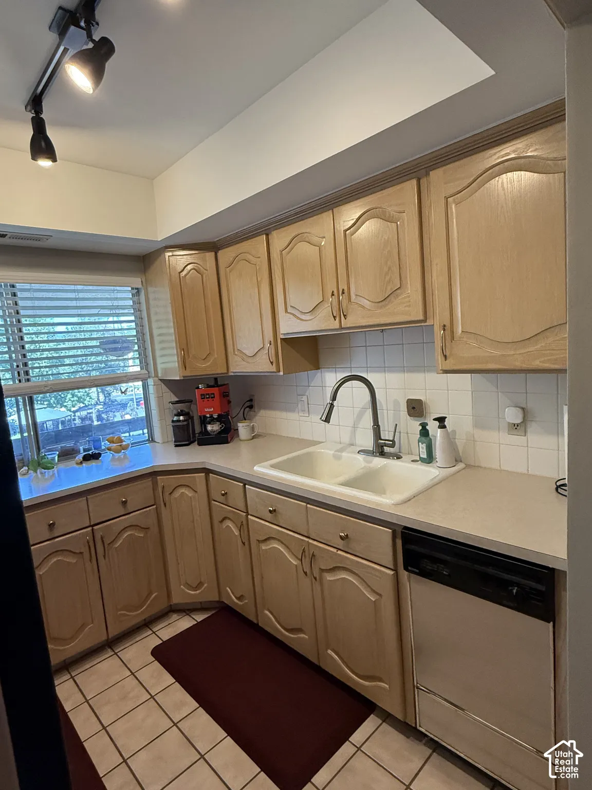 Kitchen featuring track lighting, wood-finish cabinetry, a double basin sink, neutral countertops, and a white tile backsplash