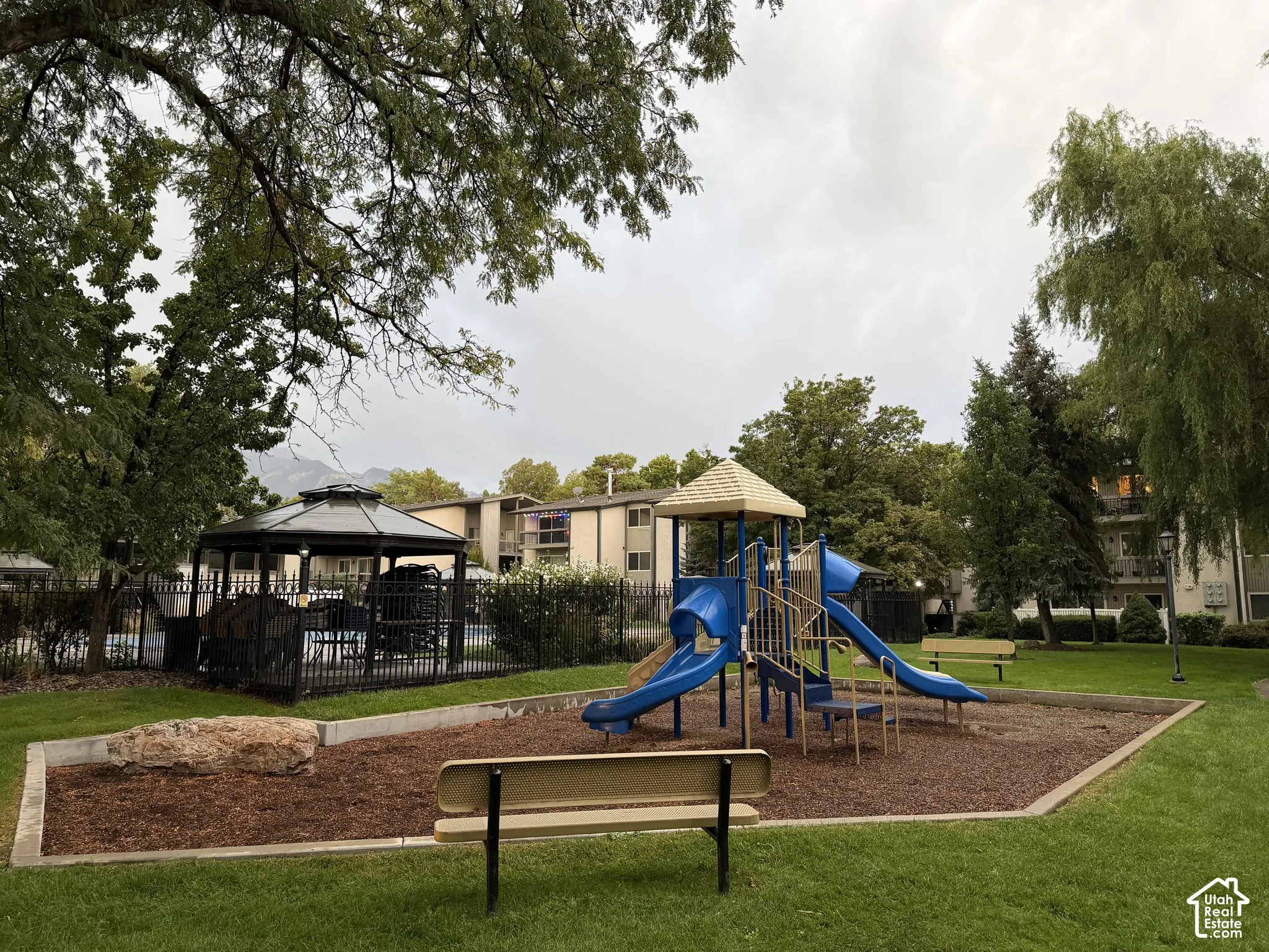 Expansive green space featuring a https://assets.utahrealestate.com/photos/280x210/hb5553198_46f70383561906ef65215a8cab50f1e1_6ab6e2ceed708_edited_1790372243.jpgplayground with slides, a covered gazebo, and mature trees