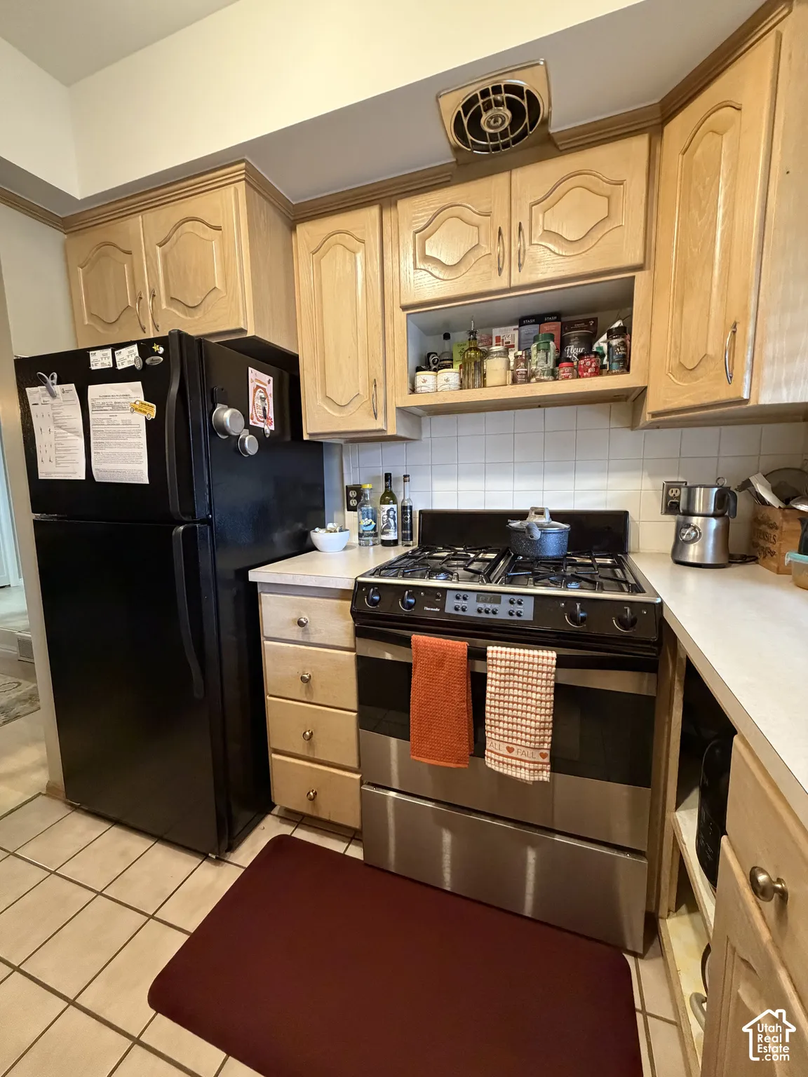 Wood-finish cabinetry with decorative panels, tile flooring, and a stainless steel gas range
