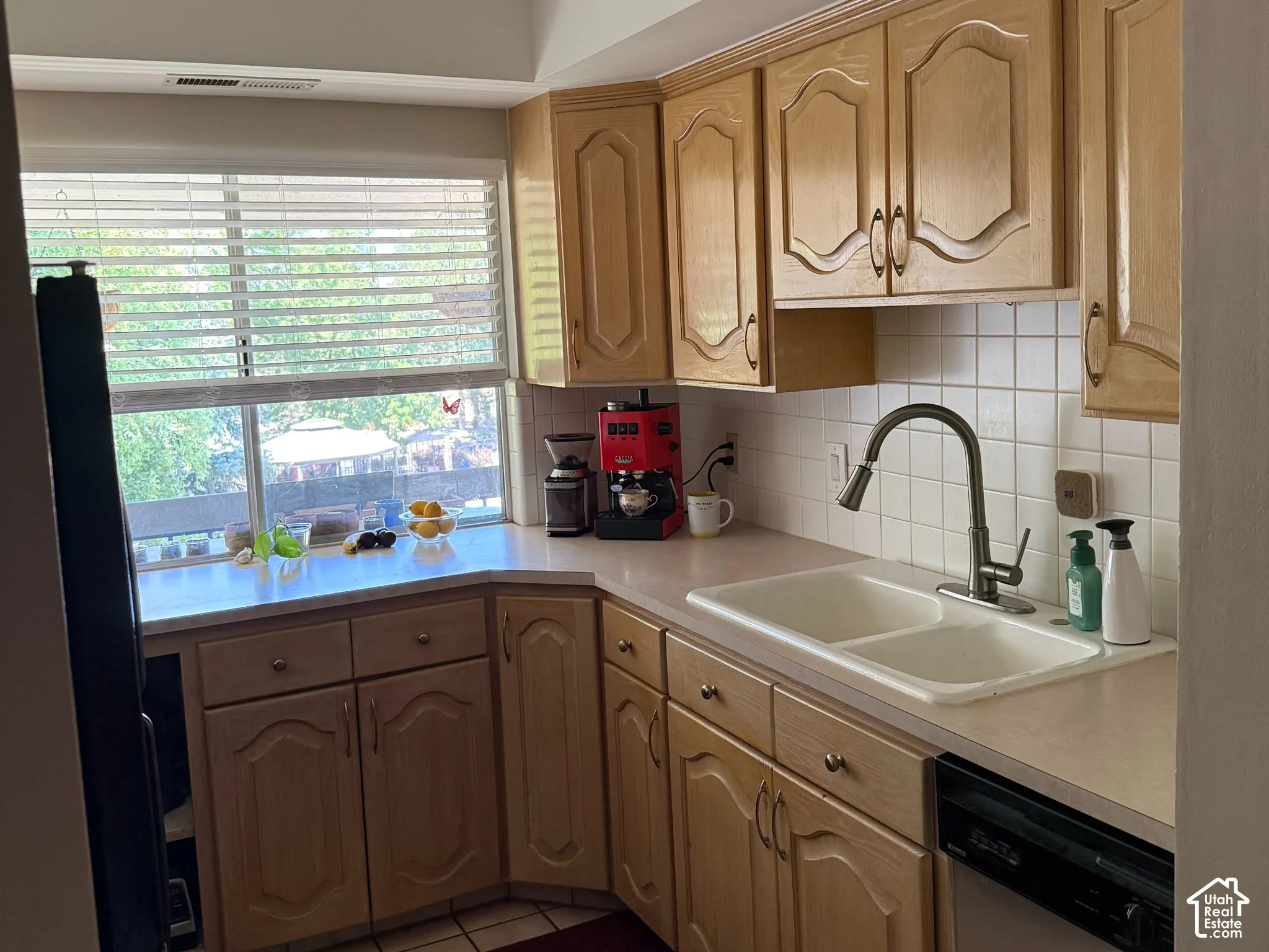 Kitchen featuring light wood cabinetry, a double basin sink, tile flooring, and a window with blinds