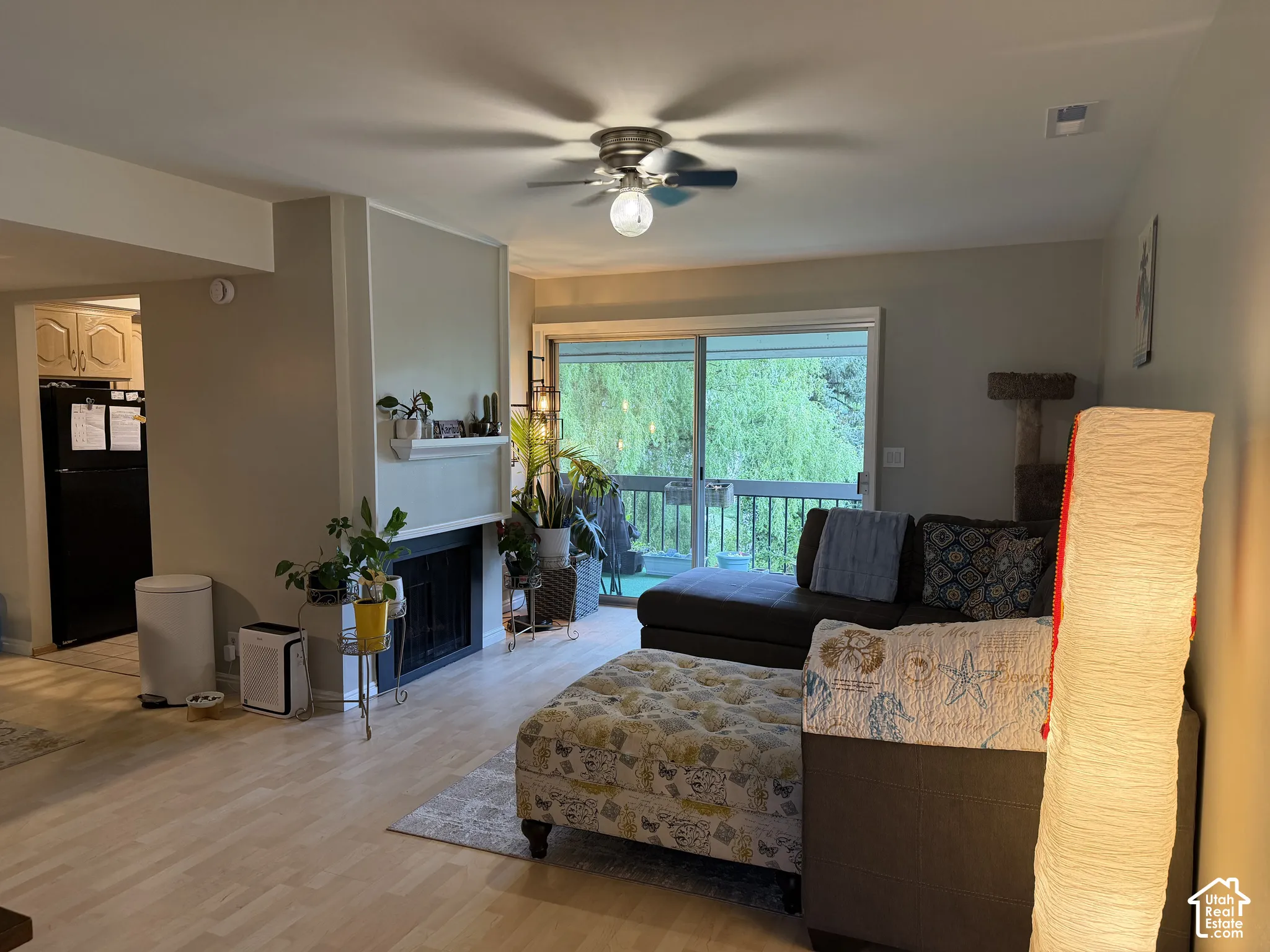 Wood-finish flooring throughout, featuring a fireplace with a white mantel, and a ceiling fan with integrated lighting