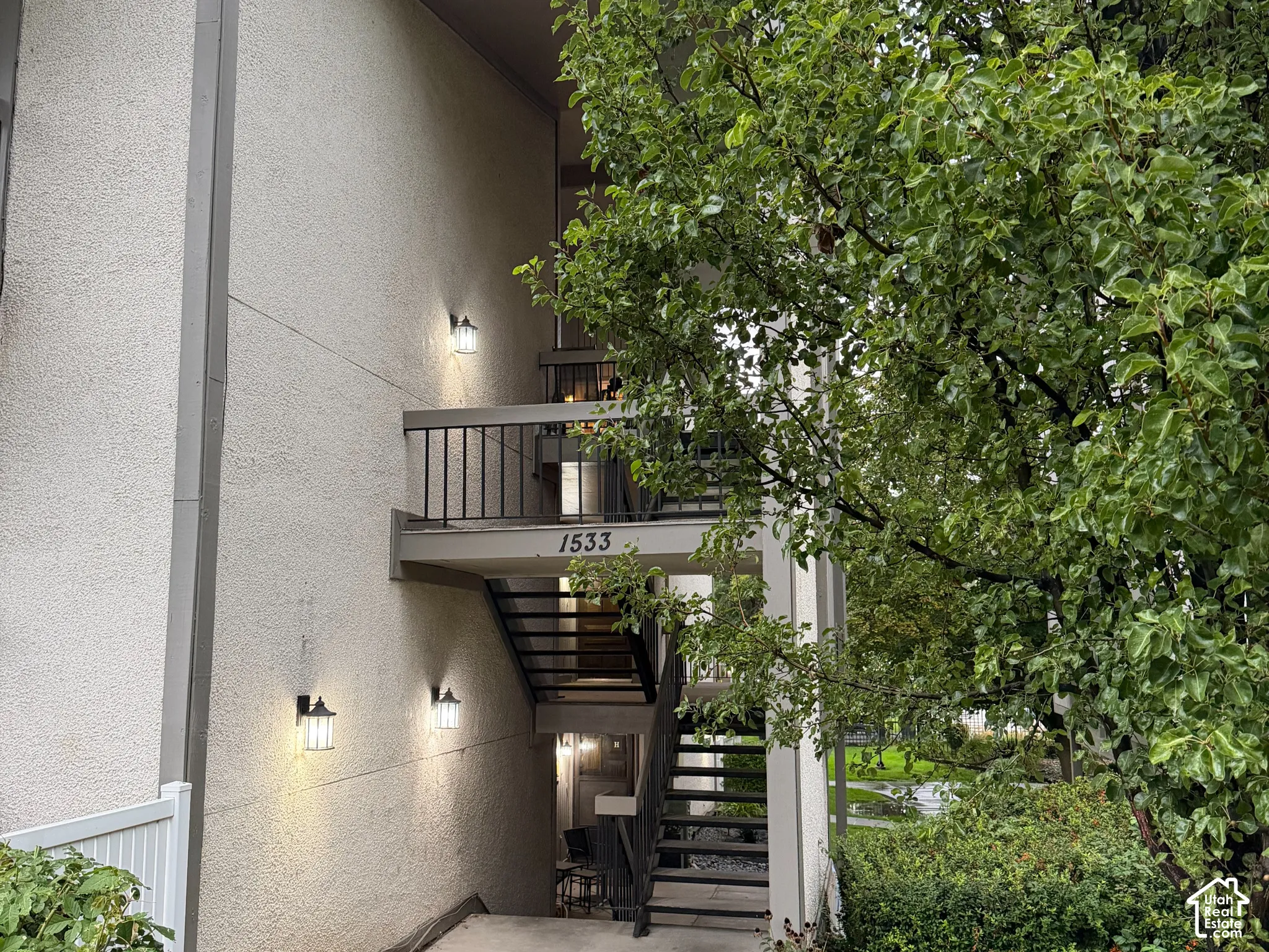 Exterior building with stucco finish, metal railing, outdoor lighting fixtures, and concrete pathway