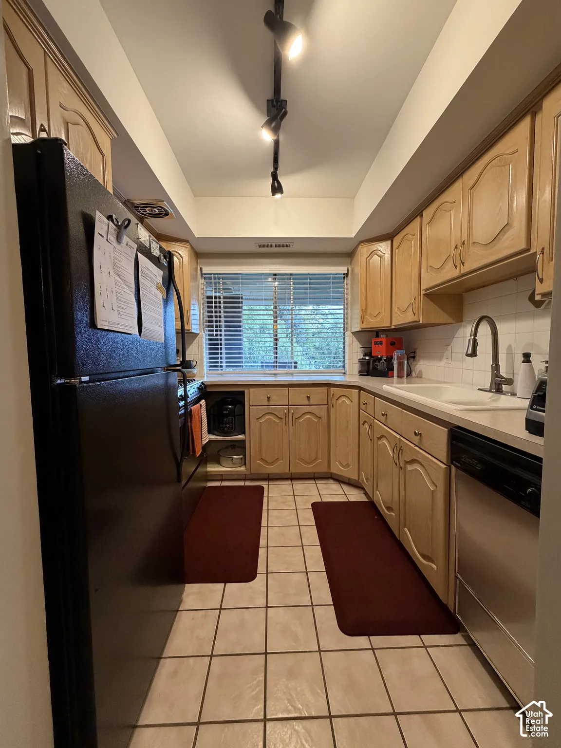 Kitchen featuring light wood cabinetry, a stainless steel dishwasher, and a white tile backsplash