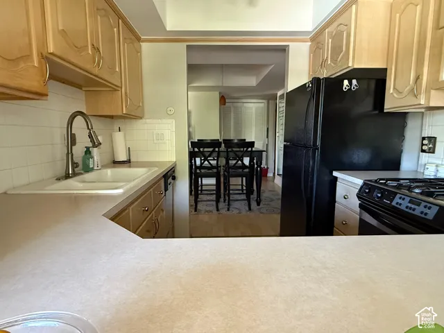 Light wood-finish cabinetry with decorative panels, white tile backsplash, and a contemporary pull-down faucet