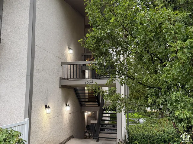Exterior building with stucco finish, metal railing, outdoor lighting fixtures, and concrete pathway