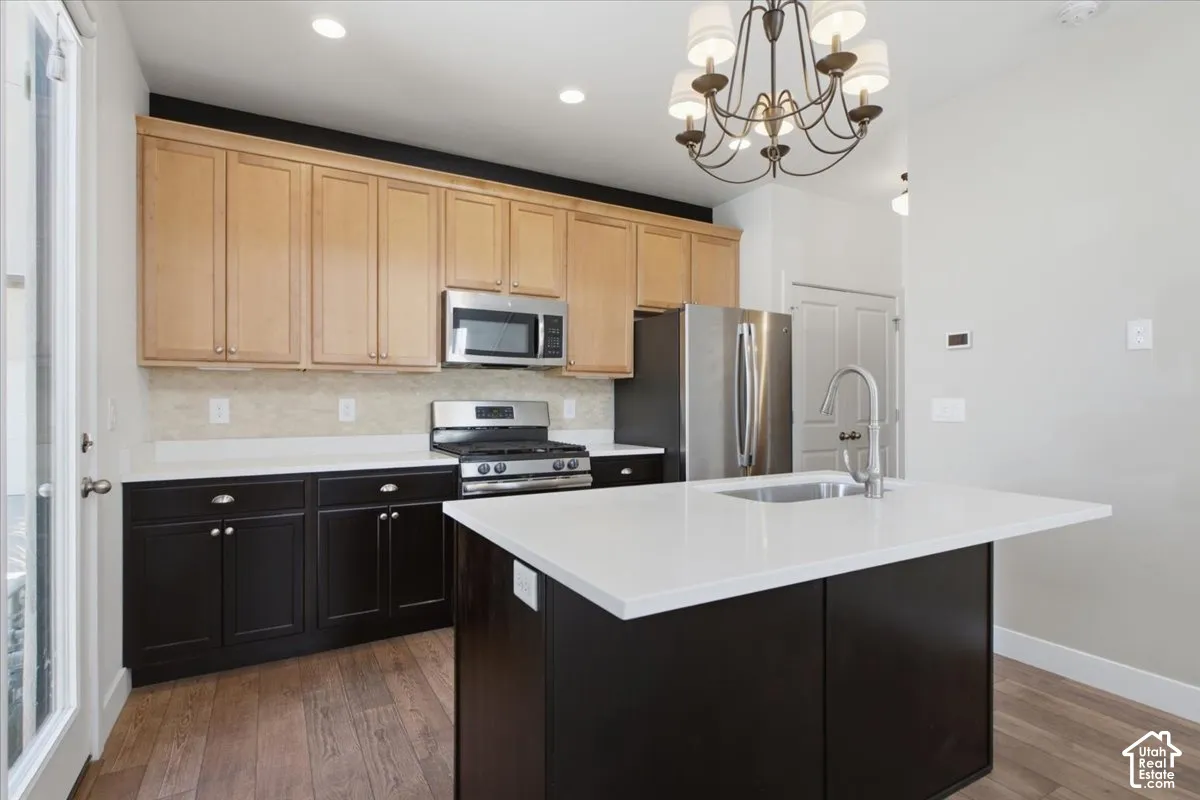 Two-tone cabinetry with stainless steel appliances, white countertops, and a kitchen island with an integrated sink