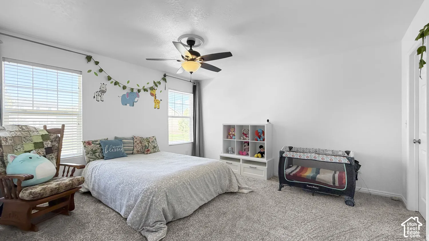 Carpeted flooring, white walls, two windows with blinds, and a ceiling fan with integrated lighting