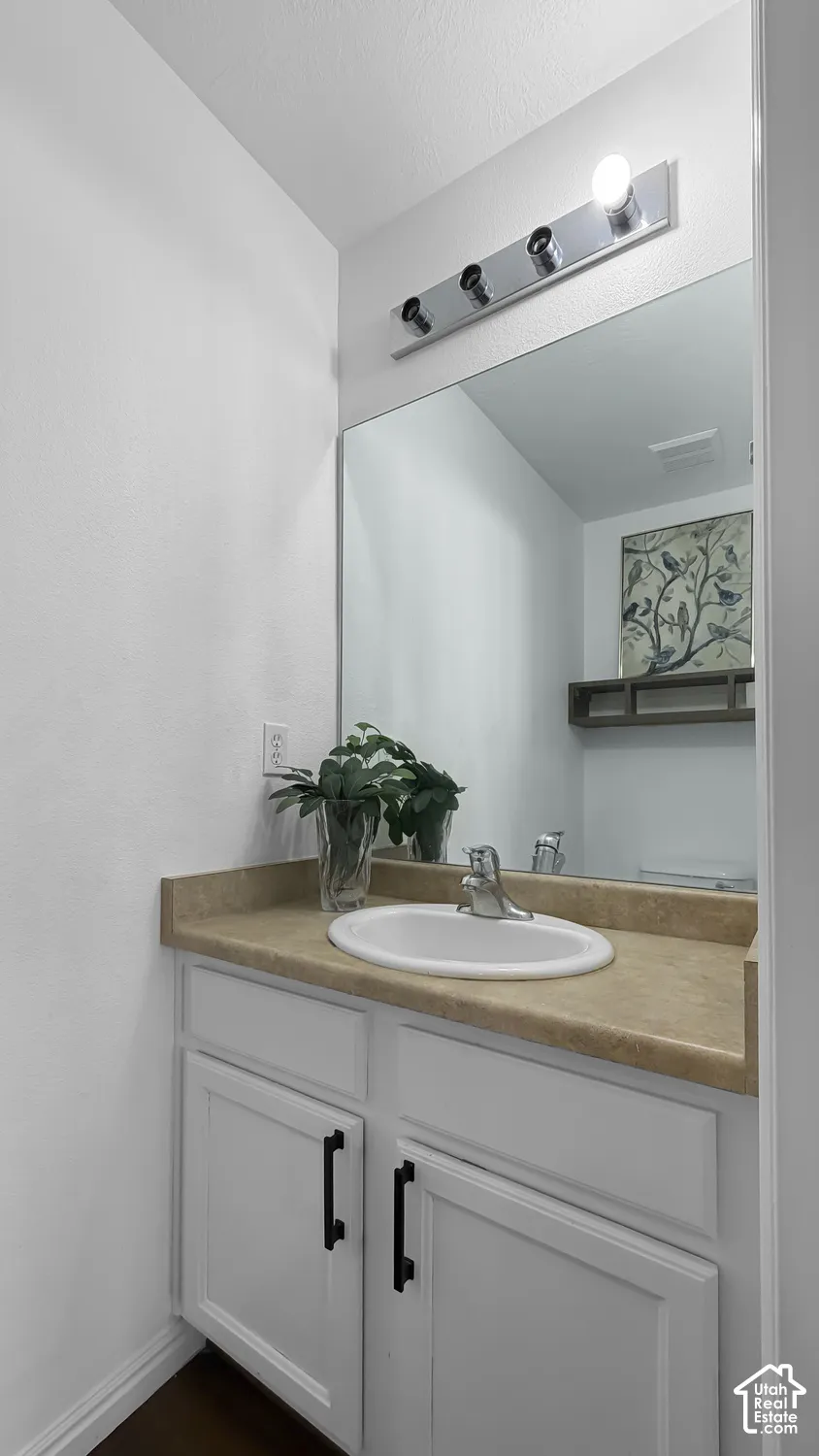 White vanity with black cabinet pulls, a single basin sink, and a light-toned countertop