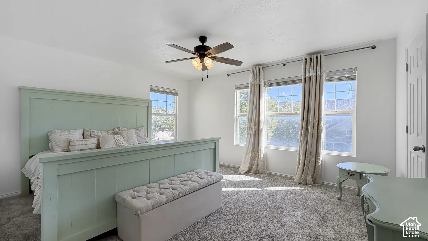 Recessed ceiling fan with integrated lighting, multiple windows with natural light, textured carpeting, and a white paneled door