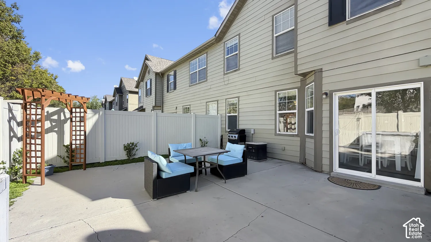 Paved patio with a wooden arbor and white privacy fencing