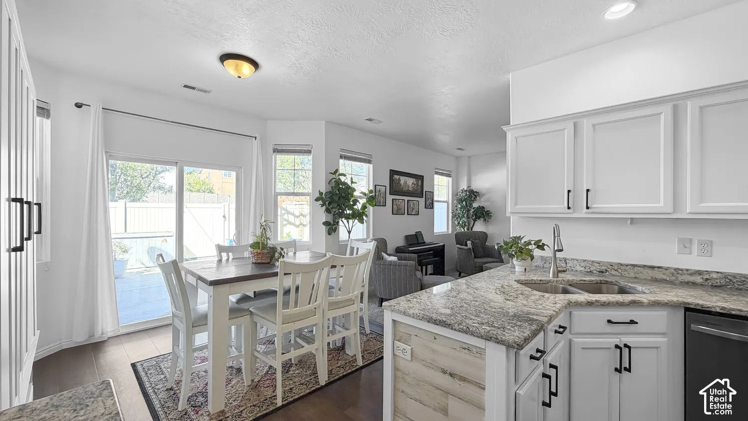 White shaker-style cabinetry with black hardware, stone countertops with an undermount sink, wood-finish flooring, and sliding glass door access to a patio