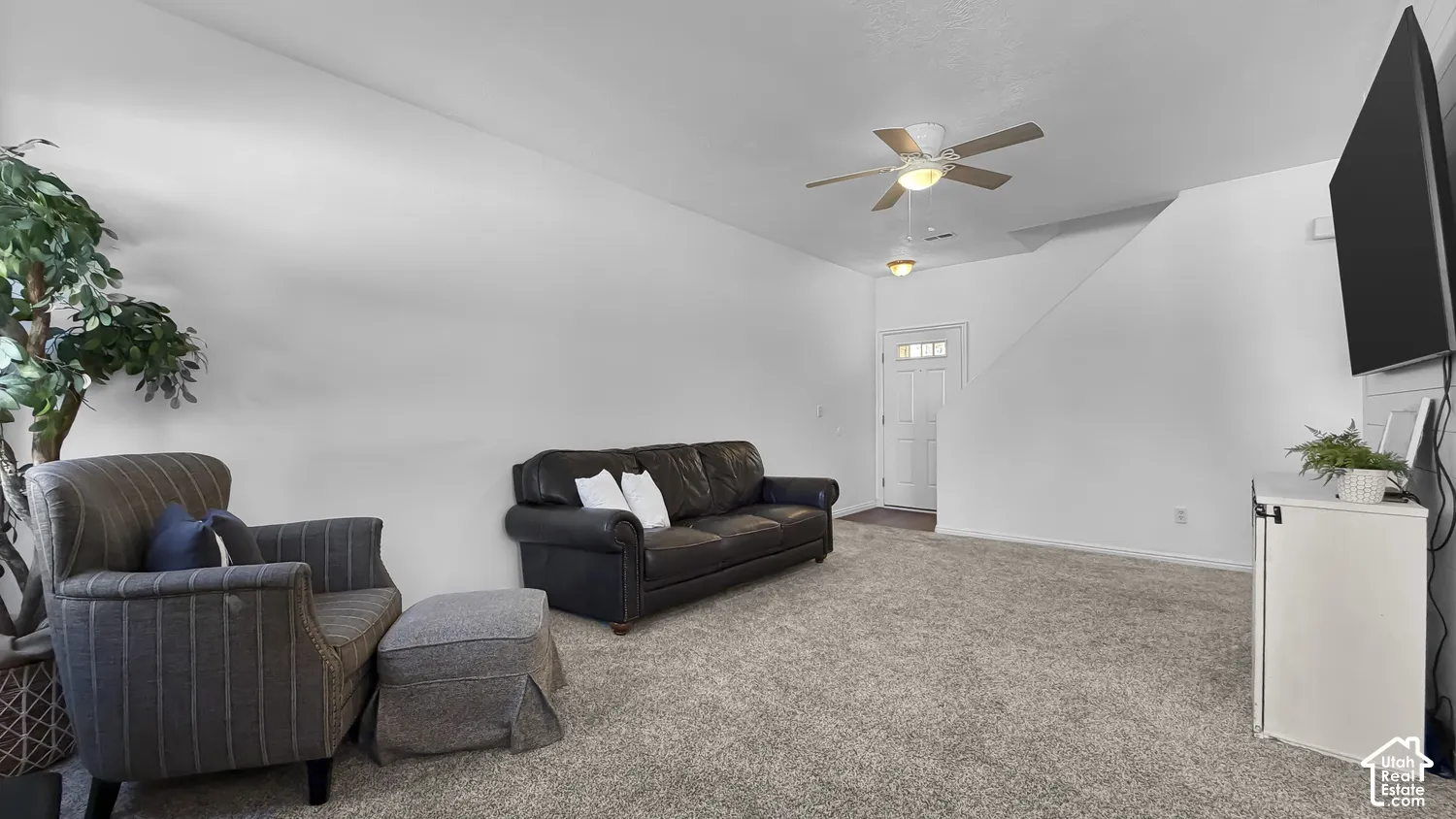 Plush carpet flooring, a ceiling fan with integrated lighting, and a front entry door with privacy glass
