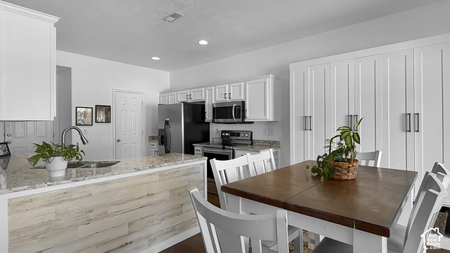 White shaker-style cabinetry with matte black hardware, stainless steel appliances, a kitchen island featuring a gooseneck faucet and stone-finish countertop, and integrated white storage cabinets